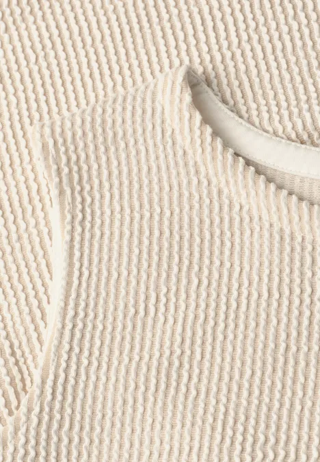 Close-up van een crèmekleurige, geribbelde gebreide top met ronde hals.