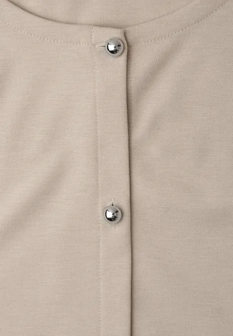 Nahaufnahme eines beigen Kleidungsstücks mit zwei silbernen Druckknöpfen in der Mitte.