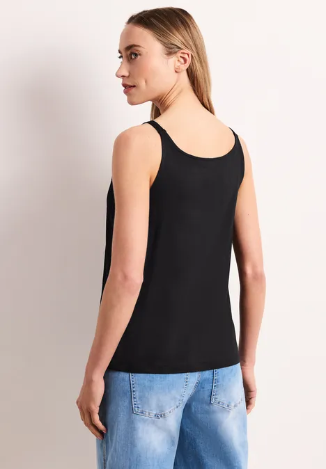 Top in structuurmix Black Achteraanzicht van een persoon in een zwart topje en spijkerbroek tegen lichte achtergrond.