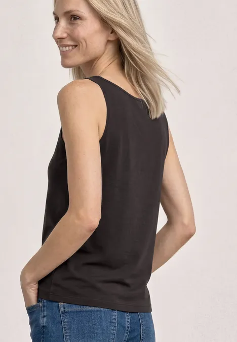 Eine Frau trägt ein schwarzes ärmelloses Top und blaue Jeans, Blick von hinten.