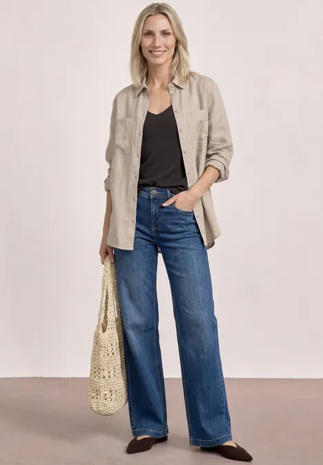 Frau trägt beige Hemdjacke, schwarzes Top, weite Jeans, gehäkelte Tasche und dunkle Schuhe.