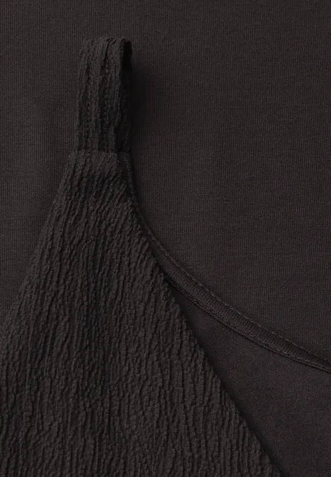 Nahaufnahme eines schwarzen Oberteils mit feiner, gerippter Struktur an einem Träger.