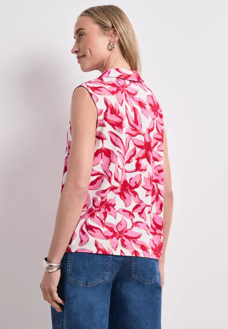 Vrouw gezien van achteren met mouwloze roze-witte top met bloemmotief en een spijkerbroek.