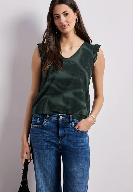 Vrouw in groene mouwloze top, blauwe jeans, met een kleine zwarte handtas