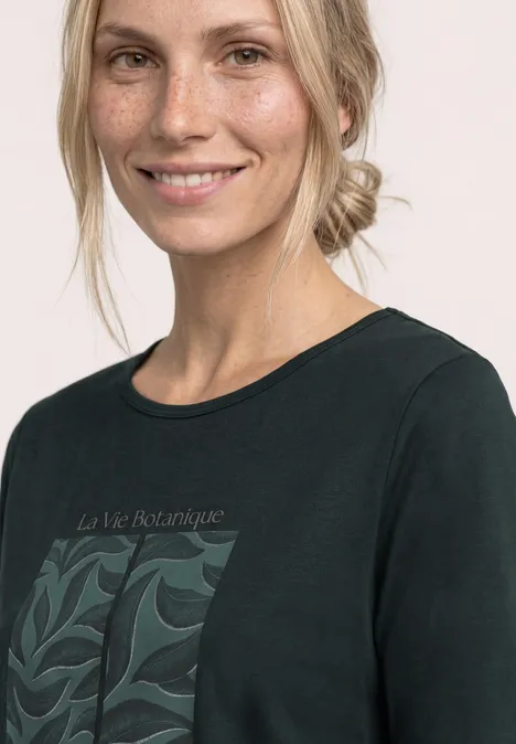 Een vrouw draagt een zwart T-shirt met botanisch motief en de tekst "La Vie Botanique".