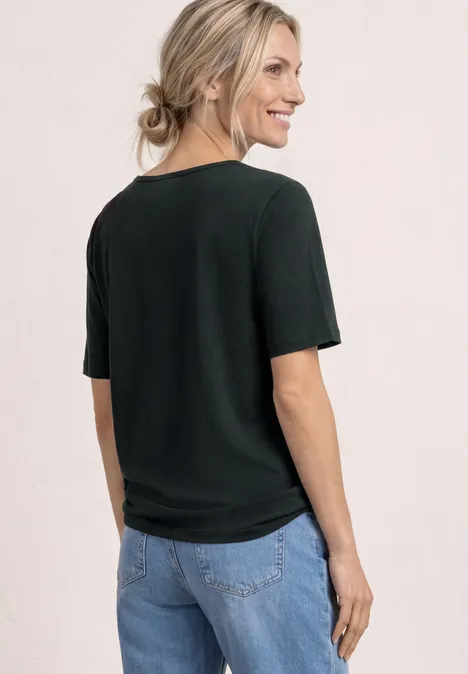 Vrouw van achteren met zwart T-shirt en spijkerbroek, blonde haren in een losse knot.