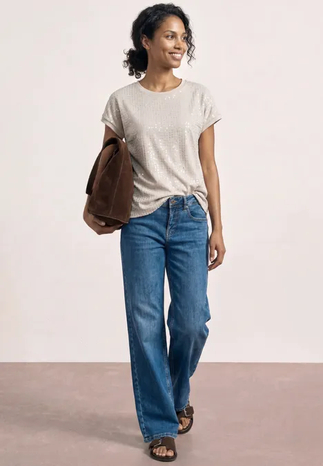 Personne en t-shirt blanc, jean bleu et sandales, tenant une veste marron sous le bras.