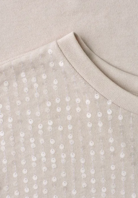 Pull beige à col rond orné de paillettes brillantes disposées en rangées sur le devant.