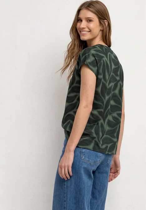 Frau von hinten in dunkler Bluse mit Blattmuster und blauen Jeans.