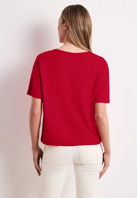 Vrouw van achteren met een rood T-shirt en een witte broek.