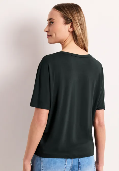 Achteraanzicht van vrouw met halflang blond haar in eenvoudig zwart T-shirt.