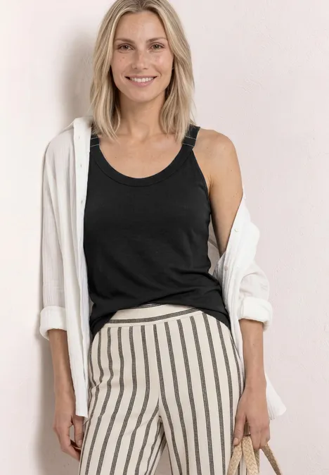 Vrouw met zwarte top, witte blouse los over de schouders en gestreepte broek, met een tas in de hand.