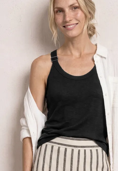 Vrouw met vervaagd gezicht draagt zwart tanktop, witte overshirt en gestreepte broek.