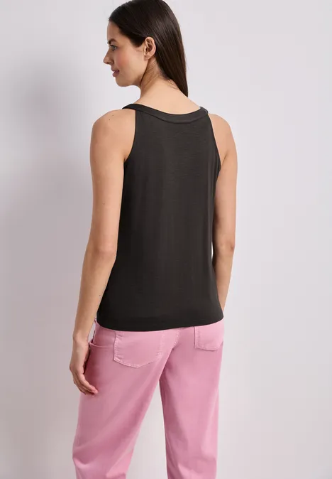 Vrouw, rugzicht, draagt zwart mouwloos top en roze broek voor lichte achtergrond.