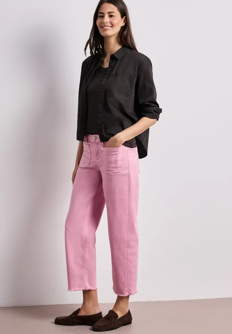 Iemand draagt een zwart overhemd en roze rechte broek tegen een eenvoudige achtergrond.