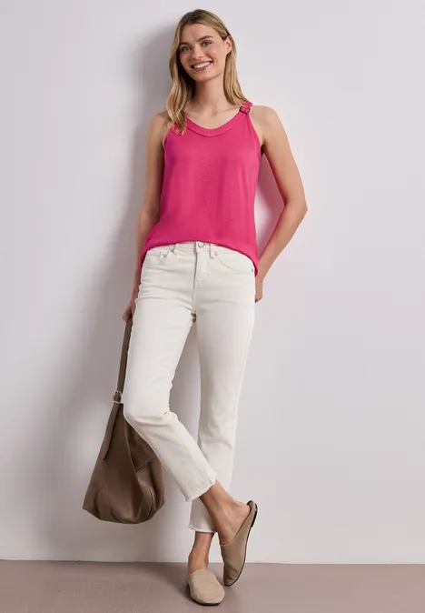 Vrouw in roze hemdje, witte jeans en beige loafers met bijpassende tas tegen neutrale achtergrond.