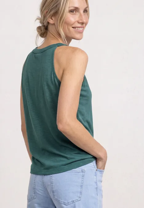 Top mit V-Neck und Deko-Detail mediterra green Eine Frau in grünem ärmellosem Top und hellblauer Jeans, lächelnd mit den Händen in den Taschen.