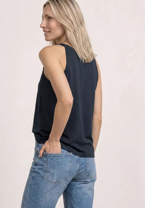 Eine Person von hinten in ärmellosem Top und Jeans, Hände in den Gesäßtaschen.