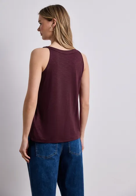 Vrouw van achteren in een bordeaux tanktop en blauwe jeans, halflang blond haar.
