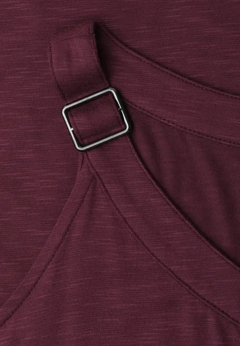 Close-up van een bordeaux kledingstuk met verstelbare band en vierkante metalen gesp.