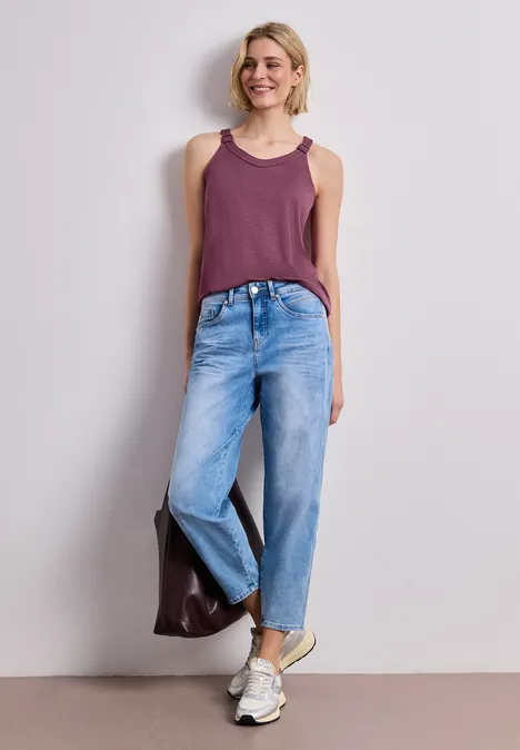 Eine Frau in einem lila Top, weiten Jeans und weißen Sneakern trägt eine braune Tasche.