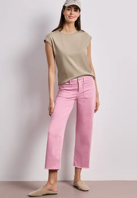 Shirt mit Boatneck und Deko-Detail timeless beige Frau trägt beige ärmellose Bluse, rosa gerade geschnittene Jeans und beige Slipper vor hellem Hintergrund.