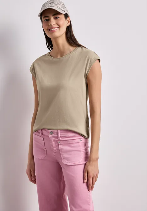 Shirt mit Boatneck und Deko-Detail timeless beige Eine Frau trägt ein ärmelloses beiges Top und rosa Jeans vor neutralem Hintergrund.