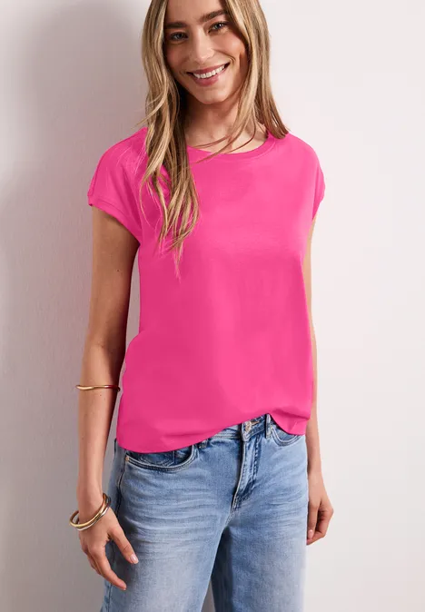 Frau in pinkem T-Shirt und Jeans vor weißem Hintergrund