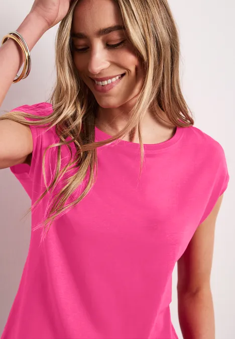 Frau steht seitlich, trägt pinkes T-Shirt und Armband, lange blonde Haare über die Schultern.