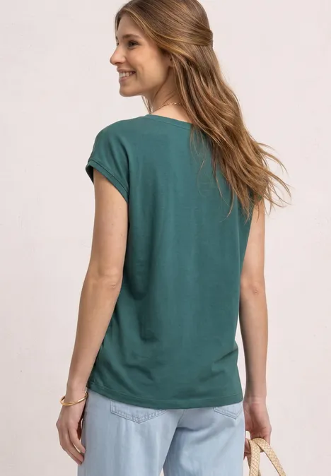 Vrouw van achteren in een groen shirt en spijkerbroek voor een lichte, neutrale achtergrond.