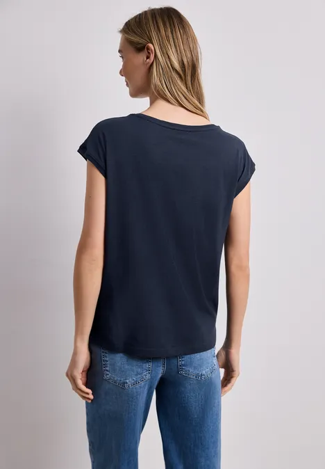 Frau von hinten in schwarzem T-Shirt und blauen Jeans vor neutralem Hintergrund