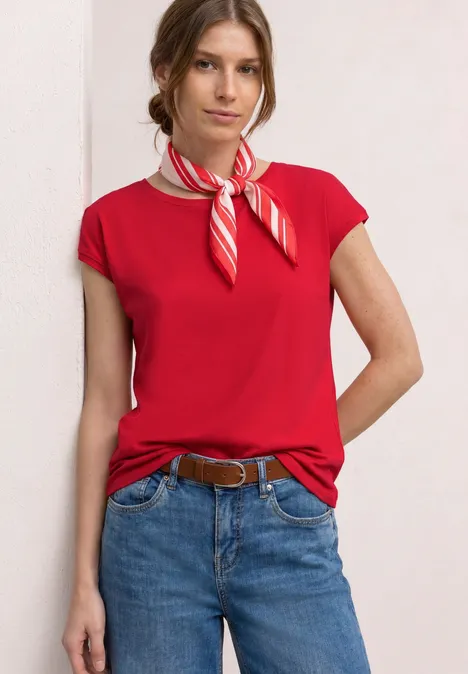 Vrouw in rood t-shirt, spijkerbroek, riem en rood-wit gestreept sjaaltje.