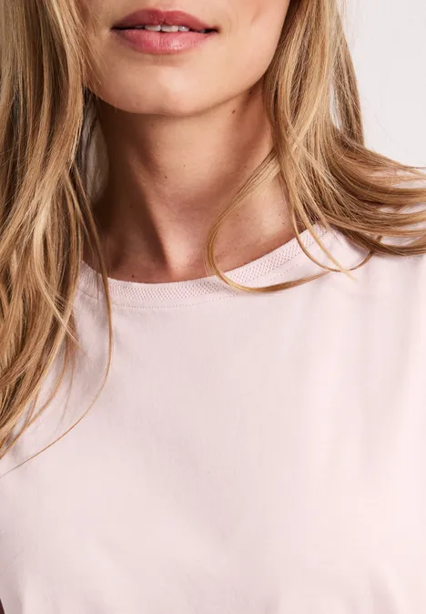 Close-up van een blonde vrouw in een roze T-shirt, enkel de hals en lippen zichtbaar.