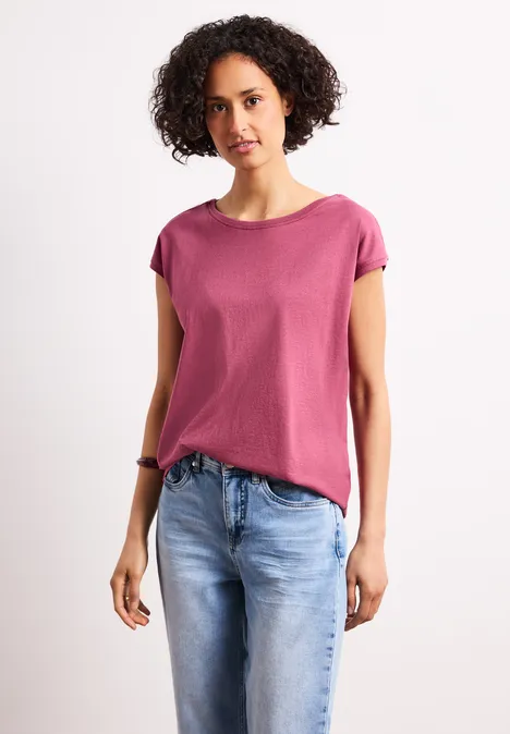 Persoon met roze T-shirt en blauwe spijkerbroek voor een witte achtergrond.