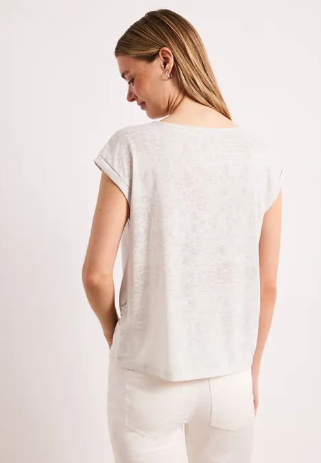 Femme de dos portant un t-shirt en lin clair et un pantalon blanc avec poches arrière.