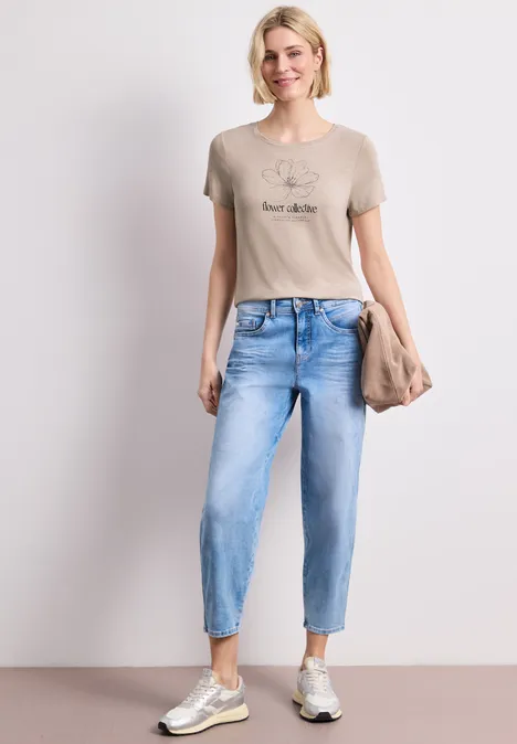 Frau in lässigem Outfit: T-Shirt, hellblaue Jeans, Sneaker und Clutch.