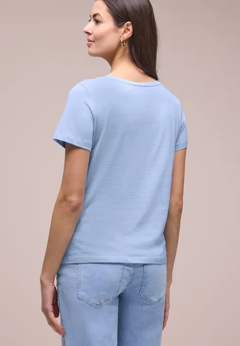 Shirt met schelpenprint cashmere blue Vrouw van achteren in lichtblauw T-shirt en spijkerbroek voor neutrale achtergrond.