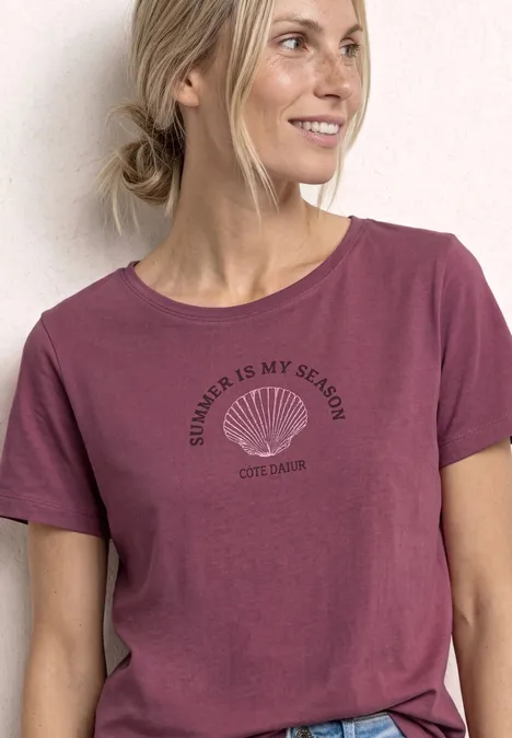 Persoon draagt roze T-shirt met schelpmotief en tekst 'Summer is my season'.