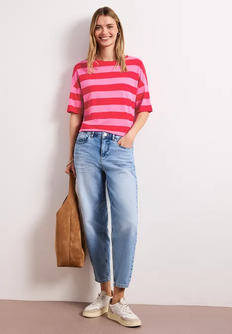 Shirt met ronde hals en strepen salsa red Een vrouw draagt een roze-rood gestreept shirt, lichtblauwe jeans, witte sneakers en een bruine tas.