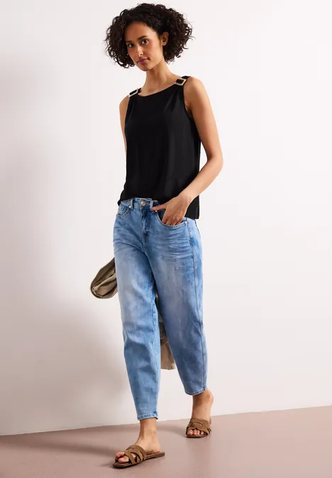 Vrouw in een zwart mouwloos topje met schouderbandjes, blauwe jeans en sandalen