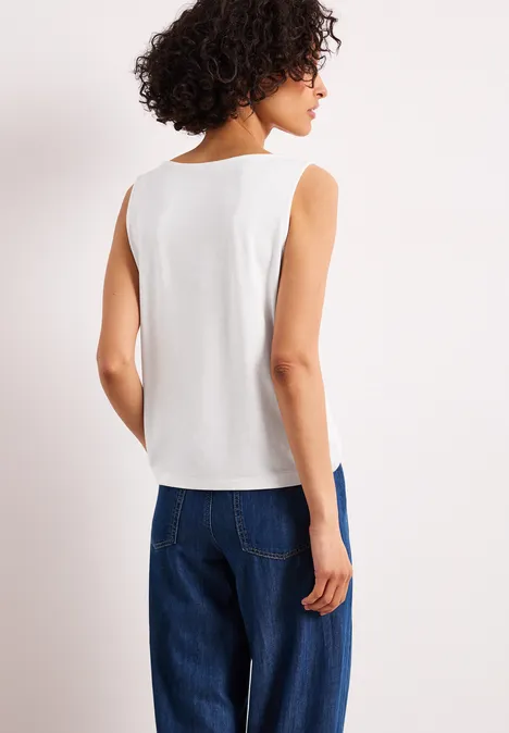 Vrouw van achteren in een wit mouwloos topje en een blauwe spijkerbroek.