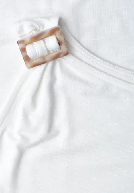 Close-up van een witte top met een vierkante, hoornkleurige gesp aan het bandje.