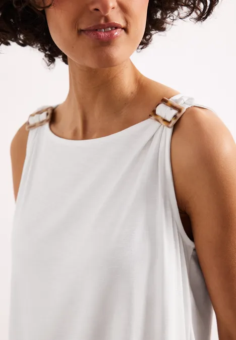 Witte mouwloze top met grote gouden gespen op de schouders.
