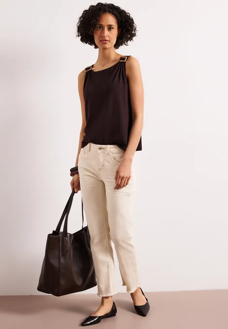 Person in schwarzem ärmellosem Top, beiger Hose und schwarzen Ballerinas mit schwarzer Ledertasche.