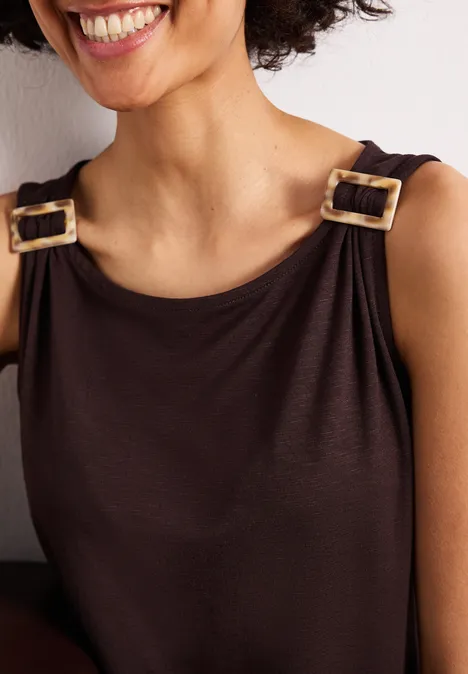 Nahaufnahme einer lächelnden Frau im braunen Top mit goldenen Schnallen an den Trägern.