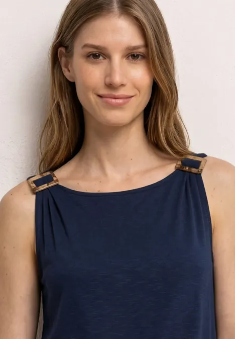 Een vrouw met een wazig gezicht draagt een mouwloze blauwe top met gouden gespen.