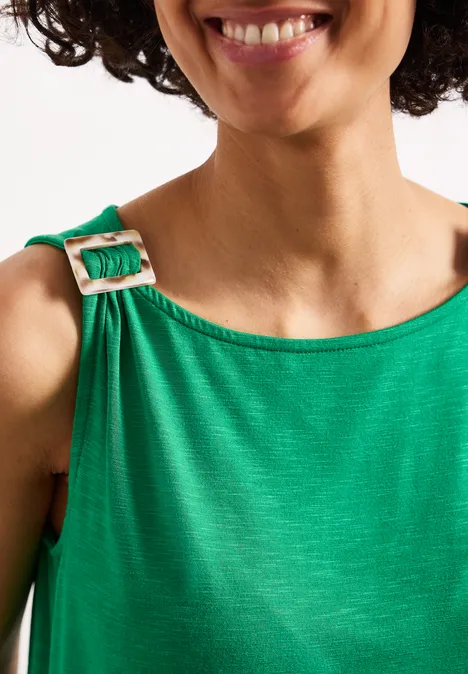 Een vrouw met krullend haar draagt een groene jurk met een schouderband en een gesp.