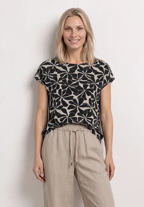 Vrouw in zwarte t-shirt met grote witte bloemenprint en beige, losse broek voor witte achtergrond