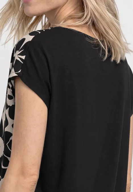 Achteraanzicht van een vrouw in een zwart shirt met beige, abstracte patronen op de mouwen.