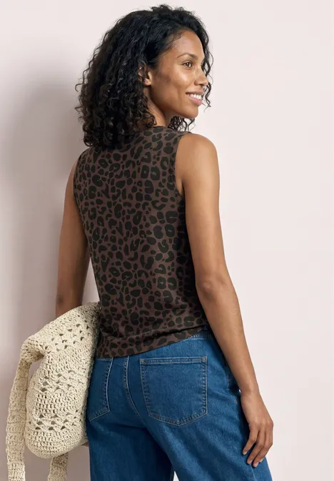 Eine Frau mit lockigem Haar trägt ein ärmelloses Leopardenmuster-Top, blaue Jeans und hält eine gehäkelte Tasche.